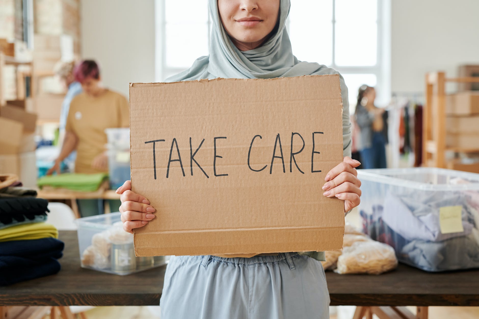 person in gray hijab holding brown cardboard with text